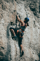 Woman climbing a rock with extreme effort in a vertical rock wall - 487085813