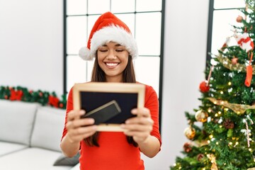 Young latin woman looking photo standing by christmas tree at home