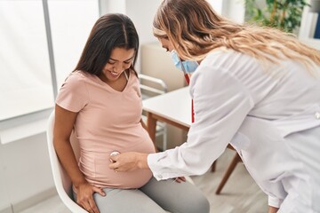 Young latin woman pregnant and doctor auscultating belly at clinic