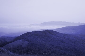 low mountains in mist toned in trendy Very Peri pantone color of the Year 2022. nature background