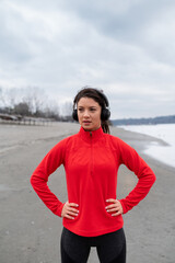 Attractive ypung runner wearing headphones listening to music while running by the river in the cold winter morning training for a marathon. Healthy lifestyle concept.