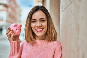 Young caucasian girl smiling happy holding piggy bank at the city.