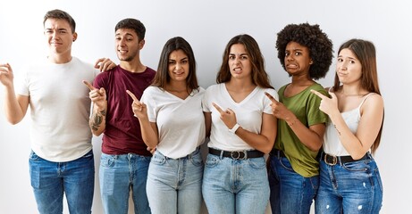 Group of young friends standing together over isolated background pointing aside worried and...