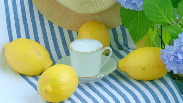 Cappuccino at the hotel on the terrace. Mediterranean cruise vacation. Italian lemons on a linen striped tablecloth, white porcelain with gold border, straw hats forgotten, blue hydrangea