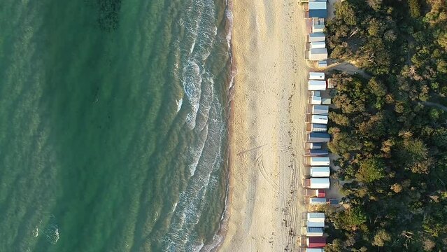 Lonely person walking along beach water front past famous multicolored beach boxes.