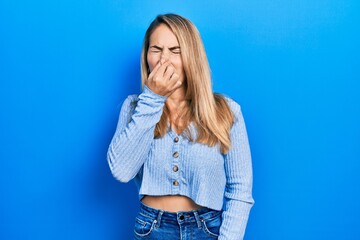 Young caucasian woman wearing casual clothes smelling something stinky and disgusting, intolerable smell, holding breath with fingers on nose. bad smell