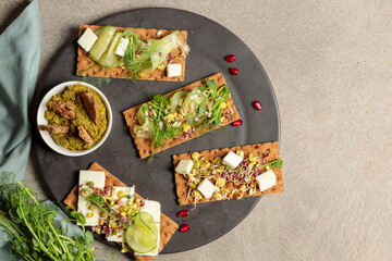 Finn crisp with pesto, microgreens, cheese or tofu on a black plate. Top view , copy of the space