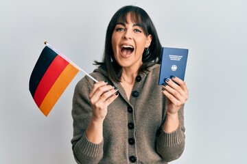 Naklejka premium Young hispanic woman holding germany flag and passport celebrating crazy and amazed for success with open eyes screaming excited.
