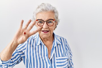 Senior woman with grey hair standing over white background showing and pointing up with fingers number four while smiling confident and happy.