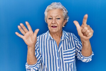 Senior woman with grey hair standing over blue background showing and pointing up with fingers number seven while smiling confident and happy.