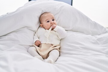 Adorable baby relaxed lying on bed with fingers on mouth at bedroom