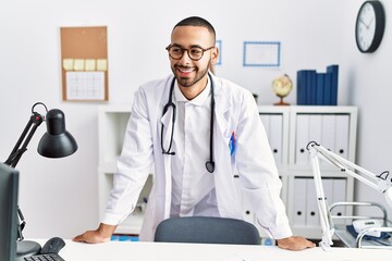 Young hispanic man smiling confident wearing doctor uniform at clinic