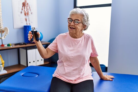 Senior grey-haired woman physitherapist patient having rehab session using hand grip at clinic