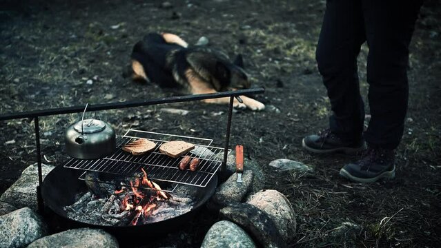 Man and dog resting near the campfire and preparing food on the campfire