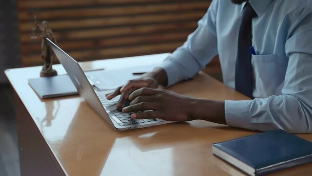 Young businessman or boss typing in front of laptop and sitting at table in company spbas. Closeup of african American man types text on computer keyboard and does work, sits at desk with statue of