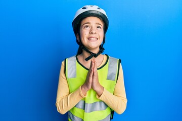Beautiful brunette little girl wearing bike helmet and reflective vest begging and praying with hands together with hope expression on face very emotional and worried. begging.