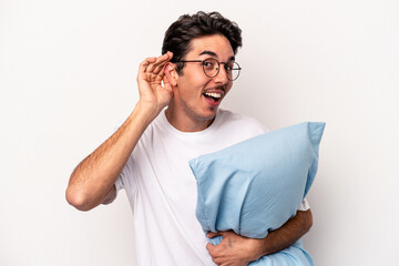 Young caucasian man wearing pajamas holding a pillow isolated on white background trying to...