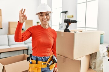 Middle age grey-haired woman wearing hardhat standing at new home smiling positive doing ok sign with hand and fingers. successful expression.