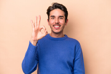 Young caucasian man isolated on beige background cheerful and confident showing ok gesture.
