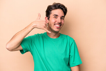 Young caucasian man isolated on beige background showing a mobile phone call gesture with fingers.