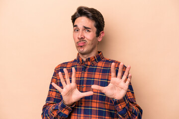 Young caucasian man isolated on beige background rejecting someone showing a gesture of disgust.