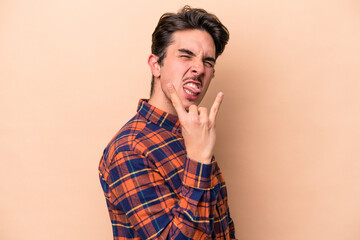 Young caucasian man isolated on beige background showing rock gesture with fingers