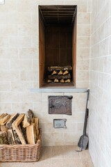 Russian wood stove. On left is basket with oak firewood. Oak firewood stacked in oven dries. In foreground at top is firebox door. Under it is ash pan door. In corner on right is poker and  scoop.