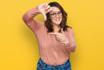 Young plus size woman wearing casual clothes and glasses smiling making frame with hands and fingers with happy face. creativity and photography concept.