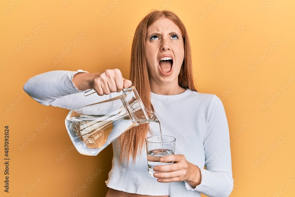 Wall mural Young irish woman pouring water angry and mad screaming frustrated and furious, shouting with anger looking up.