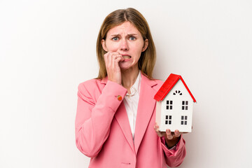 Young business English woman holding house toy isolated on white background biting fingernails,...