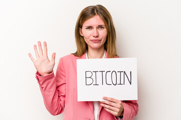 Young English business woman holding a bitcoin placard isolated on white background smiling cheerful showing number five with fingers.