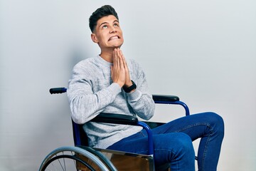 Young hispanic man sitting on wheelchair begging and praying with hands together with hope expression on face very emotional and worried. begging.