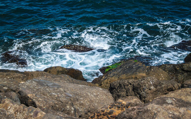 Waves on the beach, sea foam, rocky area.