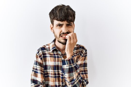 Hispanic man with beard standing over isolated background looking stressed and nervous with hands on mouth biting nails. anxiety problem.