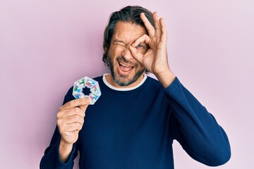 Middle age handsome man holding pill organizer smiling happy doing ok sign with hand on eye looking through fingers