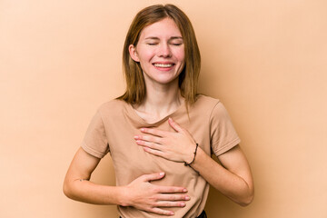Obraz premium Young English woman isolated on beige background laughs happily and has fun keeping hands on stomach.
