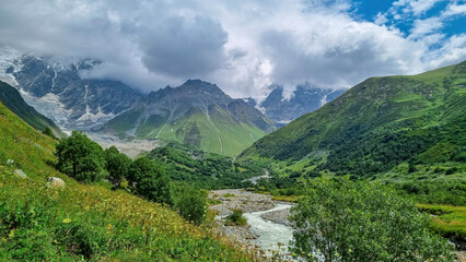 Fototapeta na wymiar Patara Enguri River flowing down the a valley with view on the Shkhara Glacier in the Greater Caucasus Mountain Range in Georgia, Svaneti Region, Ushguli. Snow-capped mountains in the back. Wilderness