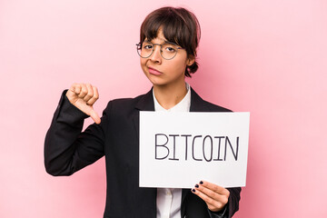 Young hispanic business woman holding a bitcoin placard isolated on pink background showing a dislike gesture, thumbs down. Disagreement concept.