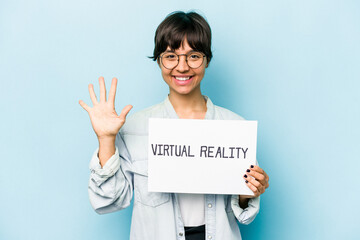 Young hispanic woman holding a virtual reality placard isolated on blue background smiling cheerful showing number five with fingers.