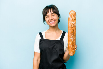 Young hispanic baker woman holding a loaf of bread isolated on blue background happy, smiling and...