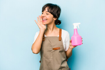 Young hispanic gardener woman holding a hand sprayer isolated on blue background shouting and holding palm near opened mouth.