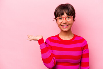 Young hispanic woman isolated on pink background showing a copy space on a palm and holding another hand on waist.