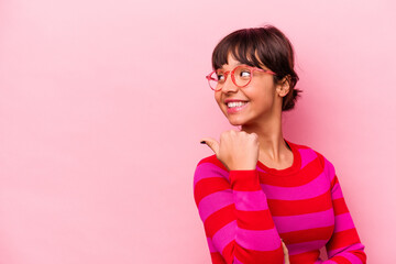 Young hispanic woman isolated on pink background points with thumb finger away, laughing and carefree.