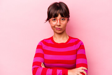 Young hispanic woman isolated on pink background frowning face in displeasure, keeps arms folded.