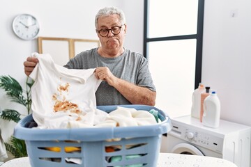 Senior caucasian man holding dirty t shirt with stain smiling looking to the side and staring away thinking.