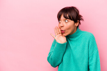 Young hispanic woman isolated on pink background is saying a secret hot braking news and looking aside