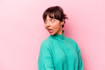 Young hispanic woman isolated on pink background looks aside smiling, cheerful and pleasant.