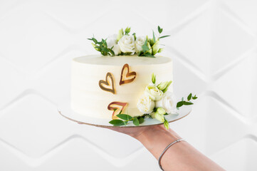 Wedding cake with floral decor on marble background. Woman holding a birthday cake, close-up
