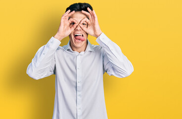 Young hispanic business man wearing business clothes doing ok gesture like binoculars sticking tongue out, eyes looking through fingers. crazy expression.