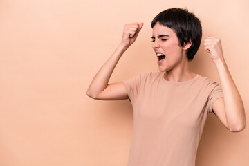 Young caucasian woman isolated on beige background raising fist after a victory, winner concept.